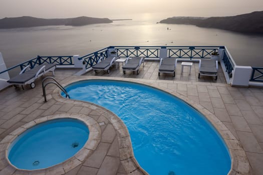 Sun loungers and pools on terrace in the village of Imerovigli with amazing view of sunset over caldera in Santorini. Greece