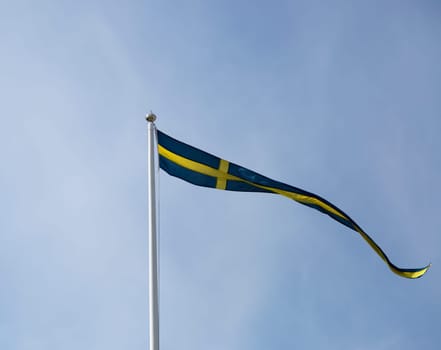 Swedish Pennent Waving on Flagpole with blue sky behing it.