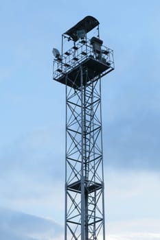 High lighting tower with observation platform at the top against a blue sky with clouds.