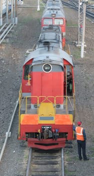 Shunting locomotive standing on rails at the train station. Nearby stands a railway worker in overalls. Front view from the top.