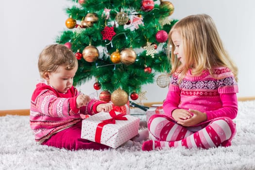 Happy children open Christmas presents on the floor and tree with New Year decoration at home.