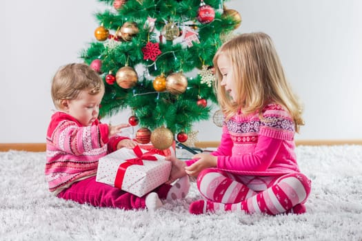 Happy children open Christmas presents on the floor and tree with New Year decoration at home.