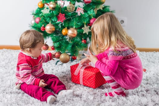 Charming happy children open Christmas presents on the floor and tree with New Year decoration at home.