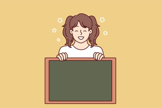 Little girl smiling demonstrates empty chalkboard designed for applying notifications or promotional offers. Preteen girl with advertising chalkboard advises to pay attention to space for text