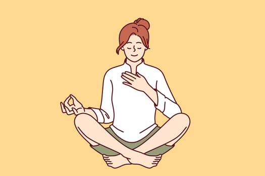 Woman meditates with hand on heart and wishes to heal herself through yoga and Buddhist spiritual practices. Girl sitting in lotus position takes care of heart chakra and relaxes during yoga