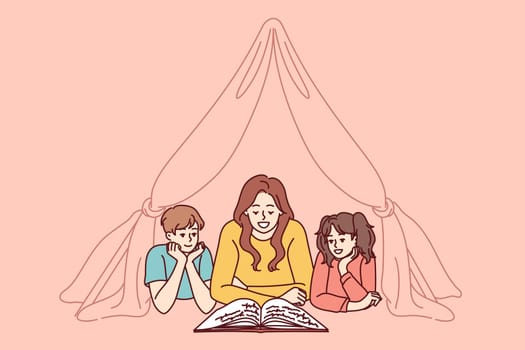 Nanny and two small children reading book lying on floor in tent enjoying fairy tale story. Mom spends time with pre-adolescent children and gets positive emotions from self-parenting