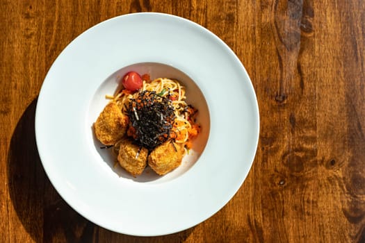 Top view of fusion spaghetti topped with ebiko and seaweed Attached with fried breaded meat. in a white round plate on a wooden table There was sunlight shining through the window. Selective focus.