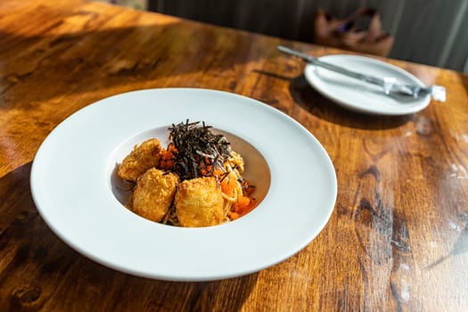 Fusion spaghetti topped with ebiko and seaweed Attached with fried breaded meat. in a white round plate on a wooden table There was sunlight shining through the window. Selective focus.