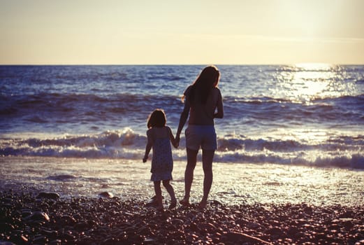 Mother with child girl at the sea beach on sunset