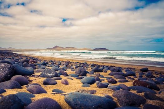 View on Famara Beach in Lanzarote, Canary Islands, Spain, with rocks in the foreground and ocean waves in the background.