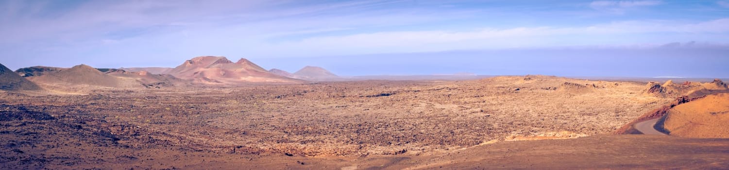 Wide panorama view on the desolate volcanic and moonlike landscape of Timanfaya National Park on Lanzarote, one of the Canary Islands of Spain and a famous travel destination for holidays