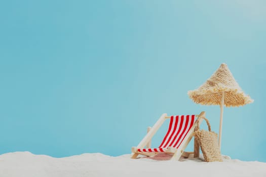Vacation, beach, travel, relaxation concept. Symbolic background with beach sand, shell, mini sun lounger, beach chair, wooden lounge, beach bag, blue sky, sea or ocean. Minimalism with copy space