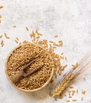 Bowl of raw dry rye grain with a wooden spoon on white table top view. Healthy alternative low gluten seeds. Protein source for vegan and vegetarian diet.