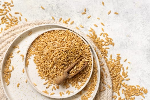 Plate of raw dry rye grain with a wooden spoon on white table top view. Healthy alternative low gluten seeds. Protein source for vegan and vegetarian diet.