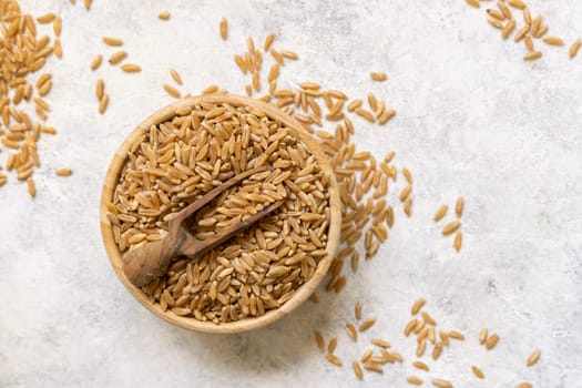 Bowl of raw dry rye grain with a wooden spoon on white table top view. Healthy alternative low gluten seeds. Protein source for vegan and vegetarian diet.
