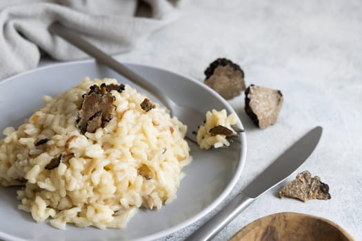 Risotto with wild porcini mushrooms and black truffles from Italy served in a plate close up on white table, copy space. Eating Italian gourmet cousine