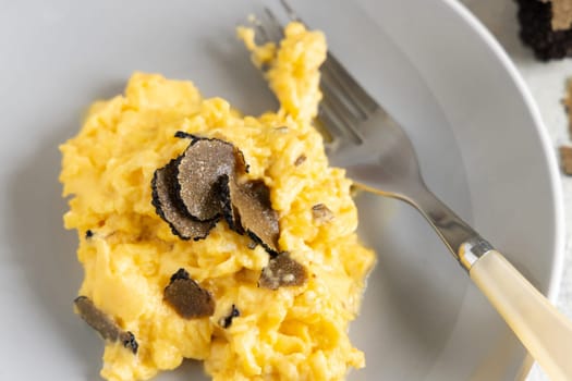 Scrambled eggs with sliced fresh black truffles from Italy served in a plate close up. Italian cousine, gourmet breakfast