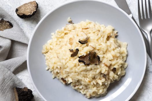 Risotto with wild porcini mushrooms and black truffles from Italy served in a plate top view on white table. Eating Italian gourmet cousine
