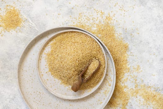 Pile of Dry uncooked bulgur wheat grain with a scoop on a plate top view, copy space. Vegetarian and Vegan, Mediterranean and Middle Eastern cuisine. Healthy lifestyle