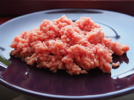 Minced meat on a purple ceramic large plate. Delicious fresh ground meat for making cutlets, steaks, hamburgers, meatballs. Pork semi-finished products.
