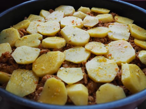 Raw potatoes, cut into circles and stacked on top of minced meat and onions. Moussaka making process. Spices on potatoes. Balkan cuisine - traditional Greek, Serbian and Turkish food.