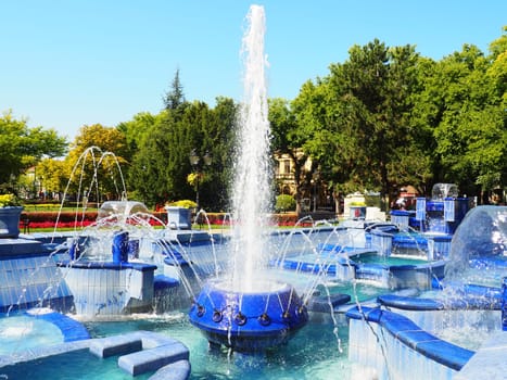 Subotica, Serbia September 12, 2021. Blue fountain in the square next to the Town Hall. Blue ceramic parts with monograms. A working fountain with splashing water. Summer sunny day by the blue water.