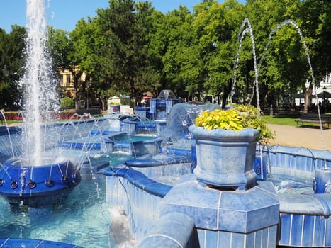 Subotica, Serbia September 12, 2021. Blue fountain in the square next to the Town Hall. Blue ceramic parts with monograms. A working fountain with splashing water. Summer sunny day by the blue water.