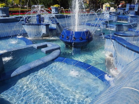Subotica, Serbia September 12, 2021. Blue fountain in the square next to the Town Hall. Blue ceramic parts with monograms. A working fountain with splashing water. Summer sunny day by the blue water.