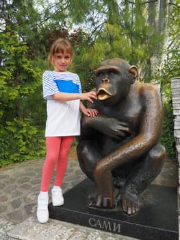 Belgrade, Serbia, April 25, 2021. A 7-year-old girl with blond hair stands next to the Sami chimpanzee statue, the symbol of the Belgrade Zoo. Inscription - Sami, monkey's nickname