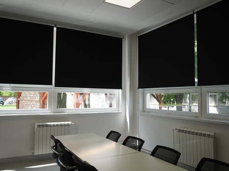 table and chairs in the meeting room in the office, in the classroom or in the library hall. White, black and gray paints in the interior. Black blinds for darkening the room. Modern interior design.