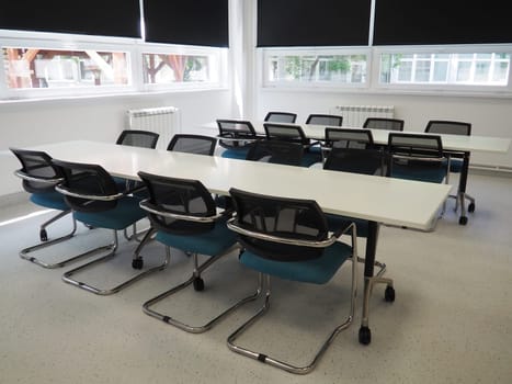 table and chairs in the meeting room in the office, in the classroom or in the library hall. White, black and gray paints in the interior. Black blinds for darkening the room. Modern interior design.