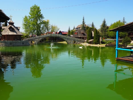 Stanisici, Bijelina, Republika Srpska, Bosnia and Herzegovina April 25, 2021 Ethno village, tourism and attractions. Stone and wood buildings and a bridge. Artificial pond with green water.