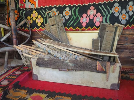 Antique carpet weaving tools. Carpet weaving in Serbia and Bosnia. Handicraft chest with wooden frames, foot spinning wheel. Log house wall with colorful carpets. Antique peasant theme. Work and hobby