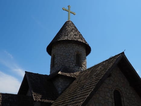 Stone Orthodox church in the ethno-park. Religious tourism. A building made of stones with a cross on the dome. Blue sky.