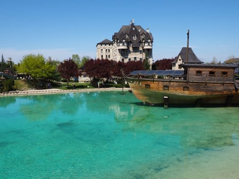 Stanisici, Bijelina, Bosnia and Herzegovina, April 25, 2021 A wooden ship with an anchor docking near the coast. Turquoise or blue water. People and tourists walk along the shore. Clear shallow water.