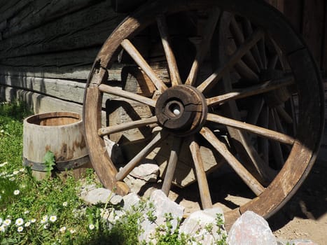 Wooden wheel from a cart. Decorative wheels for decorating lawns, exteriors and rustic interiors. Round homemade wheel against the wall. Retro or vintage style. Life in the countryside.