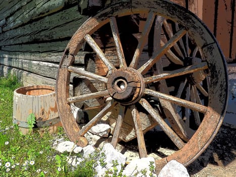 Wooden wheel from a cart. Decorative wheels for decorating lawns, exteriors and rustic interiors. Round homemade wheel against the wall. Retro or vintage style. Life in the countryside.