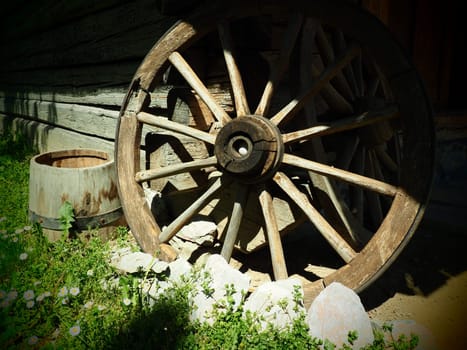 Wooden wheel from a cart. Decorative wheels for decorating lawns, exteriors and rustic interiors. Round homemade wheel against the wall. Retro or vintage style. Life in the countryside.