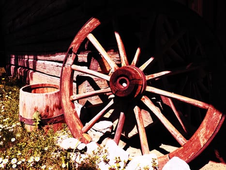 Wooden wheel from a cart. Decorative wheels for decorating lawns, exteriors and rustic interiors. Round homemade wheel against the wall. Retro or vintage style. Life in the countryside.