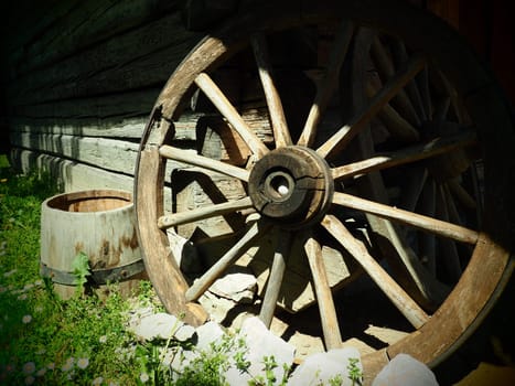 Wooden wheel from a cart. Decorative wheels for decorating lawns, exteriors and rustic interiors. Round homemade wheel against the wall. Retro or vintage style. Life in the countryside.