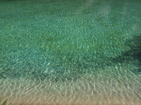 turquoise water. Clear sea water with waves and sun glare. The bottom is visible.