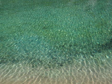 turquoise water. Clear sea water with waves and sun glare. The bottom is visible.