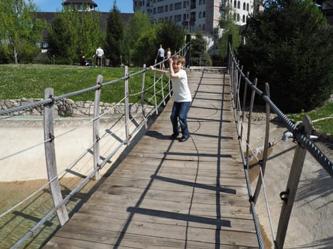 Suspended wooden bridge. The boy is trying to rock the bridge. Stanisici, Bijelina, Bosnia and Herzegovina. A bridge made of planks and railings, which can be carried by 4 people