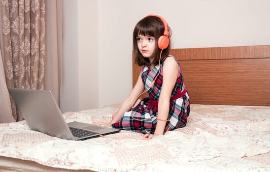 Little girl using the laptop with earphones
