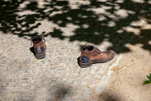 A pair of old worn brown walking shoes left behind on the path. Abandoned shoes on the way.
