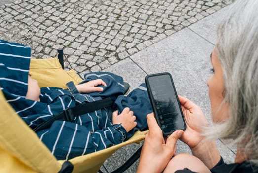 Mom uses a messenger on her mobile phone near the stroller with her sleeping son.