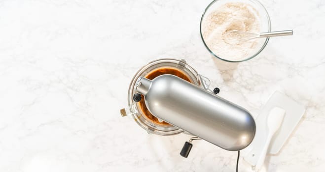 Overhead view of a baking setup for Classic Gingerbread Cookie Dough, with a stand mixer surrounded by essential ingredients. Ingredients include brown sugar, butter, flour mixture, and dark molasses in individual glass bowls, showcasing the classic components needed for this festive dough recipe.