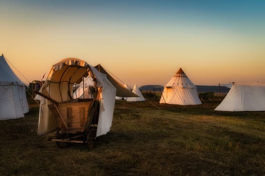Historical reenactment of Hussars, Slavic or Vikings tribe encampment with wooden cart and tent camp from 16th century at sunrise, Gniew, Poland