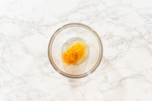Close-up top-down view of a small glass bowl filled with fresh orange zest, an essential ingredient in the Zesty Orange Gingerbread Cookie Dough recipe. The vibrant orange zest stands out against the white marble, adding a fresh, zesty touch to the recipe.