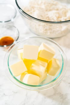 Close-up view of cubed butter in a glass bowl, ready for use in the Classic Sugar Cookie Dough recipe. The background features a mixing bowl with dry ingredients, hinting at the preparation steps for baking cookies.
